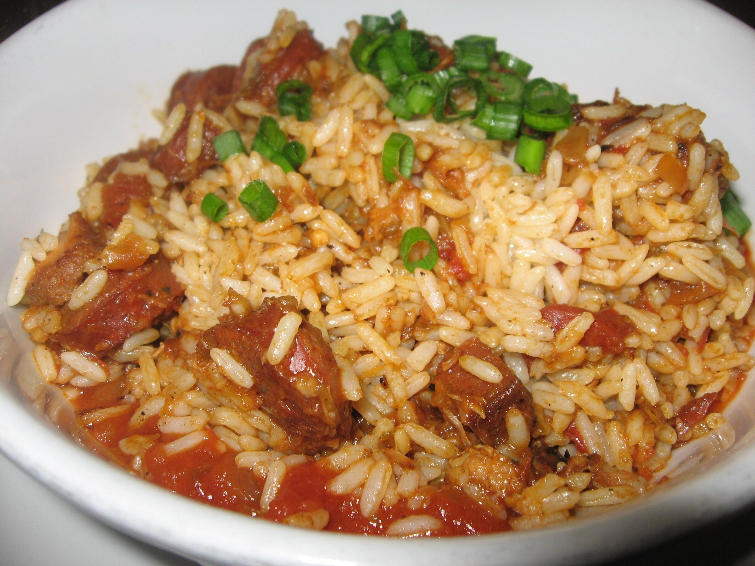 A bowl of jambalaya with sausage, rice and sliced green onions