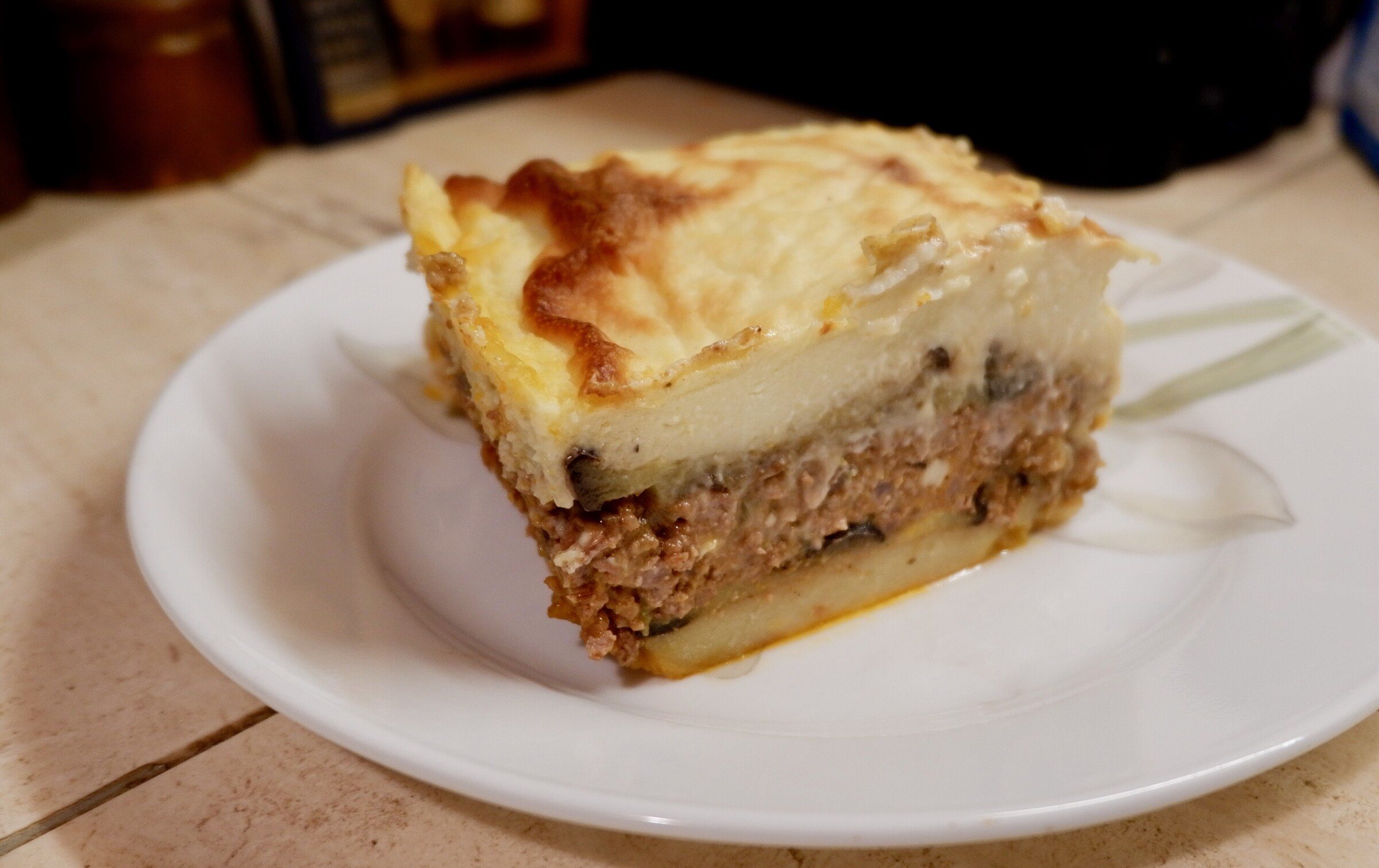 A slice of moussaka showing layers of potato, meat sauce and golden béchamel