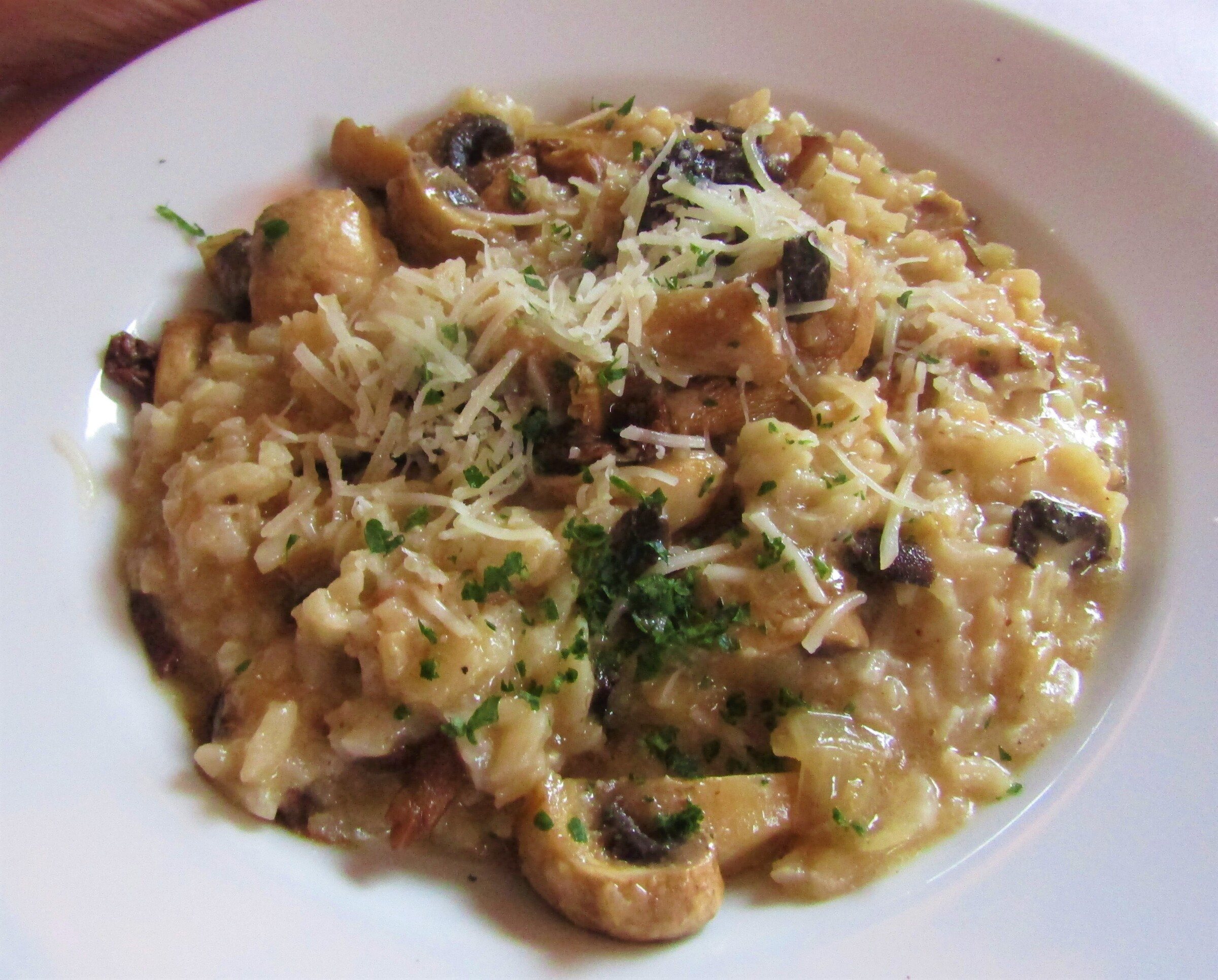 Mushroom risotto topped with grated Parmesan on a white plate