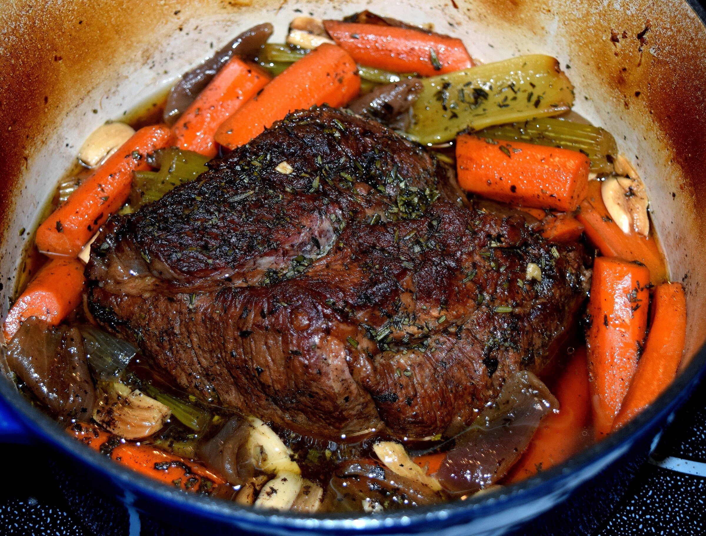 A pot roast with carrots and vegetables in a Dutch oven