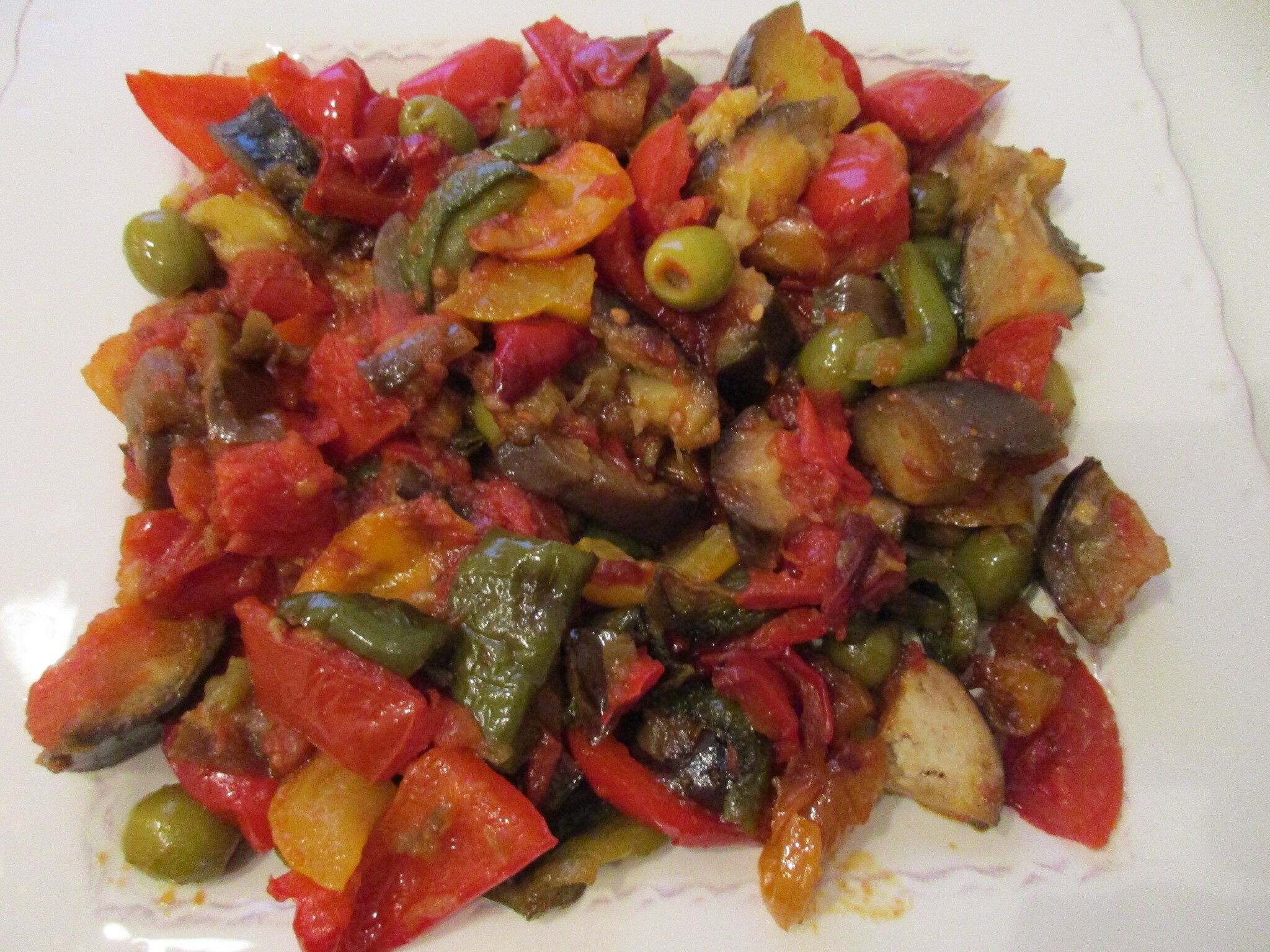 Ratatouille of peppers, eggplant, zucchini and olives on a white plate